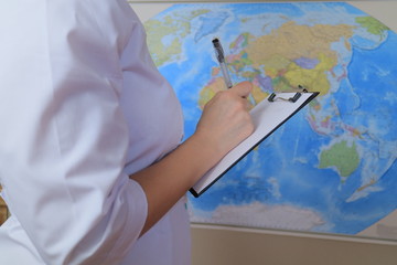 Woman doctor is writing notes on paper near global map