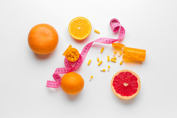Bottles with weight loss pills, citrus fruits and measuring tape on white background