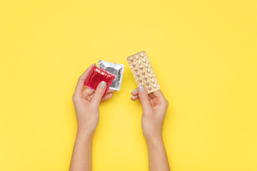 Female hands with contraceptive pills and condoms on color background