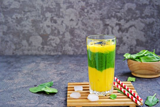 A healthy drink, a three-layer smoothie with fresh spinach and ripe mango in a tall glass glass on a dark concrete background. Drinks for detox and weight loss. Refreshing non-alcoholic cocktails.