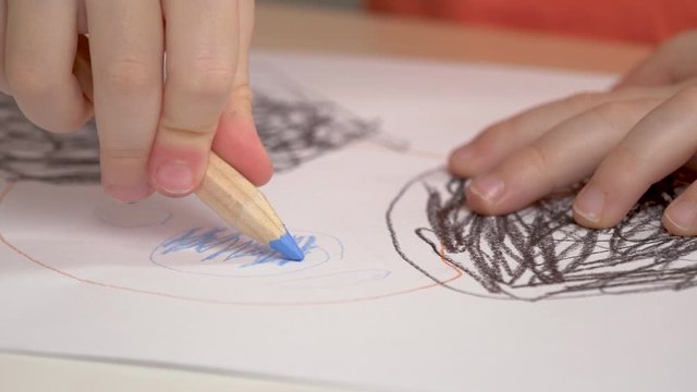 Child is drawing with colored pencils indoor. Closeup hands, picture. Children's art and crafts, training center, education, learning activities for kids concept. 