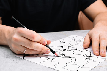 Naklejka premium Man is drawing an abstract imaginary picture of curves by a black pencil in his hand. A psychological art therapy tests. Identification of the unconscious, subconscious, the depths of the human brain.