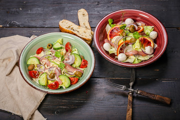 Assorted salads of traditional Mediterranean cuisine: with vegetables, salted trout, sweet onions and cheese on a dark wooden background.