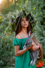 vertical portrait of a pretty teenager girl in a long green dress on a background of green foliage