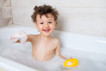 Happy baby washes in the bath holds foam in his hands and rejoices. emotional baby. hygiene...