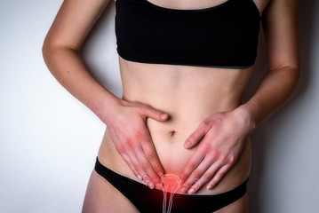 Woman suffering from stomach pain. Young woman with hands holding her crotch lower abdomen gray background.