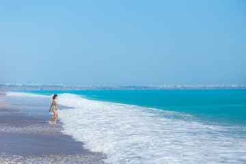 A woman in a swimsuit is walking along the sea waves.