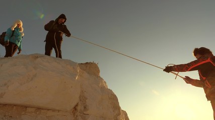 team of climbers climbs a mountain on rope. free woman helps a male traveler climb a mountain....
