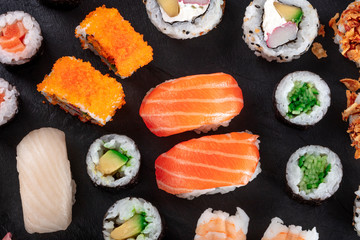 Large sushi set, shot from the top on a black background. An assortment of various maki, nigiri and rolls