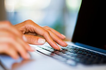 Woman typing on laptop keyboard in sunny office, business and technology concept. Close up