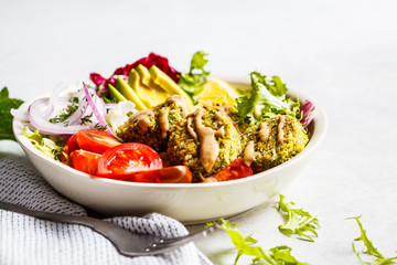 Baked falafel bowl with vegetable salad, tahini dressing and avocado.