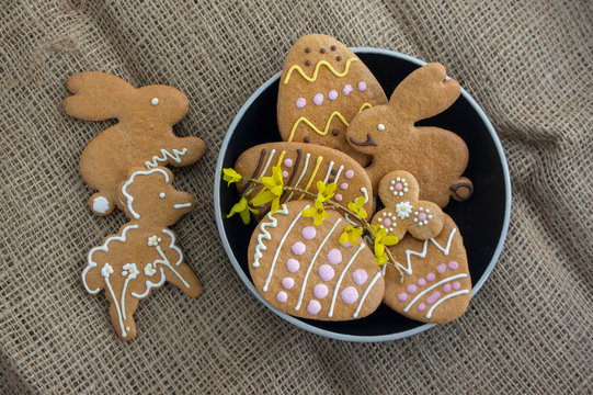 Easter holiday cookies servet on dish on the table with jute tablecloth, group of color painted gingerbread sweets springtime