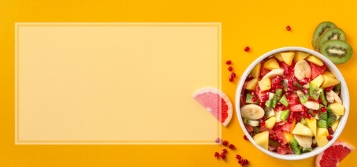 Healthy colourful fruit salad in bowl on yellow background with copy space top view Diet summer food concept