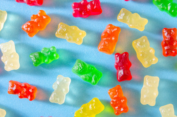 Delicious bright colored jelly bears on a blue background randomly scattered with hard shadows, top view