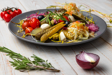 side view appetizer with homemade pickles, pickled cucumbers, garlic, onions, olives, lettuce, tomatoes, served on white wooden background, rustic style, sliced vegetables in national food restaurant