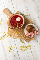 Popular dish of ukrainian cuisine Red borsch with bacon and sour cream, served on white wooden background in rustic style, top view with copy space