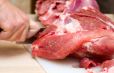 A man cuts fresh meat pork on a white Board