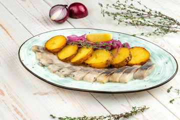 homemade salting herring with baked potatoes, red onion rings in oil and rye bread croutons, lunch menu of national food restaurant on white wooden background in rustic style