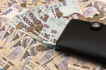 The thick money-laden black men's wallet lies against the backdrop of Ukrainian hryvnia money.