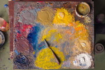 Oil paints of various colors and painters knife on a colorful palette