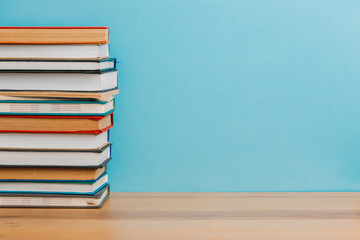 A simple composition of many hardback books, raw books on a wooden table and a bright blue background. Going back to school. Copy space. Education.