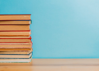 A simple composition of many hardback books, raw books on a wooden table and a bright blue background. Going back to school. Copy space. Education.