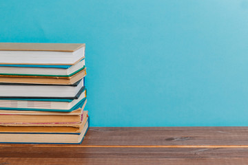 A simple composition of many hardback books, raw books on a wooden table and a bright blue background. Going back to school. Copy space. Education.