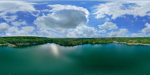 Drone Aerial 360 Degree panoramic view over the water of a large lake with stone shores. Colorful sky panorama with white clouds and a blue sky. Incredibly beautiful landscape