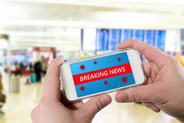 hand holds smartphone with announcement of Breaking news, Coronavirus outbreak declared pandemic in background of waiting room at airport. Concept of the spread of new coronavirus disease COVID-19