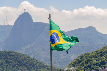 flag of brazil with image of christ the redeemer in the background in rio de janeiro.