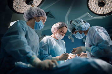 Medical team in the operating room, dark background. The theater of the operating room, an international team of professional doctors in a modern operating room are conducting an operation. Saving - Powered by Adobe