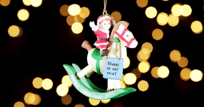 single wooden Christmas ornament of a boy on a rocking horse with out of focus lights flickering in the background, close up
