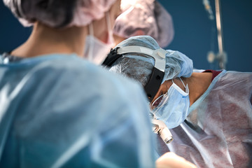 Surgical team in the operating room, close-up. An international team of professional doctors in a modern operating room is undergoing surgery. Saving lives, modern medicine, blue blue light