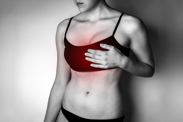 Young woman with breast pain on gray background.
