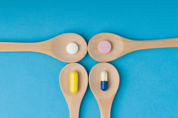  Capsules in a wooden spoons . Flat lay, top view. multi-colored tablets in a wooden spoons on a blue background.