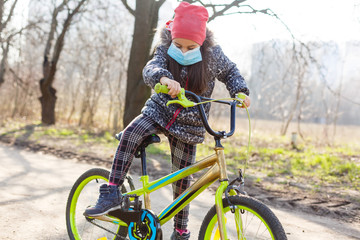 Little girl wearing anti pollution mask on her bike at park.