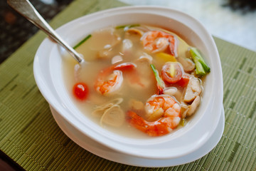 Traditional asian spicy soup tom yum in white plate on the green bamboo mat, served at the street restaurant in Thailand, Phuket