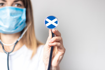 female doctor in a medical mask holds a stethoscope on a light background. Added flag of Scotland....