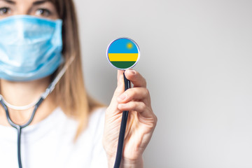 female doctor in a medical mask holds a stethoscope on a light background. Added flag of Rwanda....