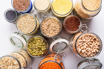 Dry grains, legumes and seeds in glass jars, top view