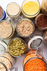 Dry grains, legumes, flakes, and seeds in glass jars, top view