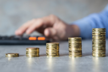 Fototapeta Oszczędności, męska dłoń licząca na kalkulatorze, monety poukładane w kolumny obraz