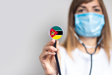 female doctor in a medical mask holds a stethoscope on a light background. Added flag of Zimbabwe....