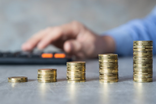 Oszczędności, męska dłoń licząca na kalkulatorze, monety poukładane w kolumny