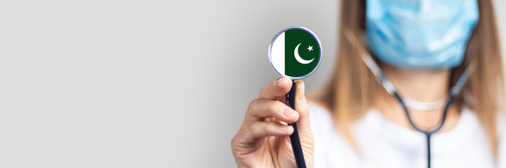 female doctor in a medical mask holds a stethoscope on a light background. Added flag of Pakistan....