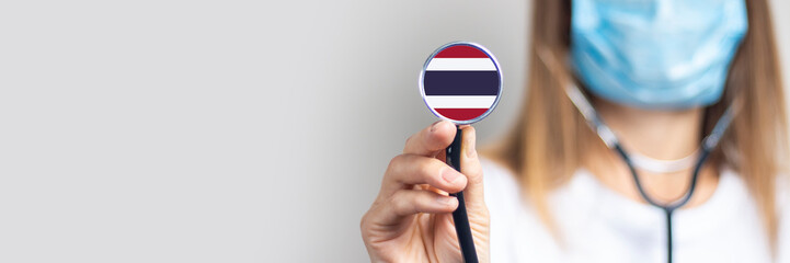 female doctor in a medical mask holds a stethoscope on a light background. Added flag of Thailand....