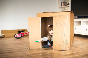 Caucasian little child looking out of a cardboard playhouse. Material recycle, eco friendly, sustainability concept, simple fun idea for entertaining children at home.