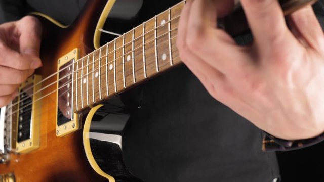 Guitarist plays a light brown six-string electric guitar with a pick against black background. Concept of stay at home and make some music. Free time for sound art. Middle shot. 4K