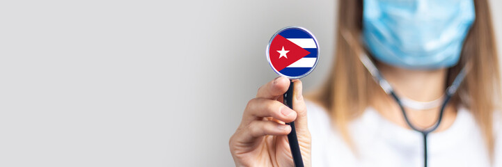 female doctor in a medical mask holds a stethoscope on a light background. Added flag of Cuba....