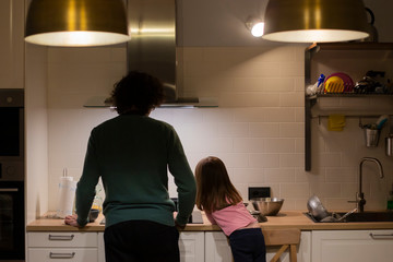 Young father and little child girl, back view, cooking together in modern white kitchen with big...